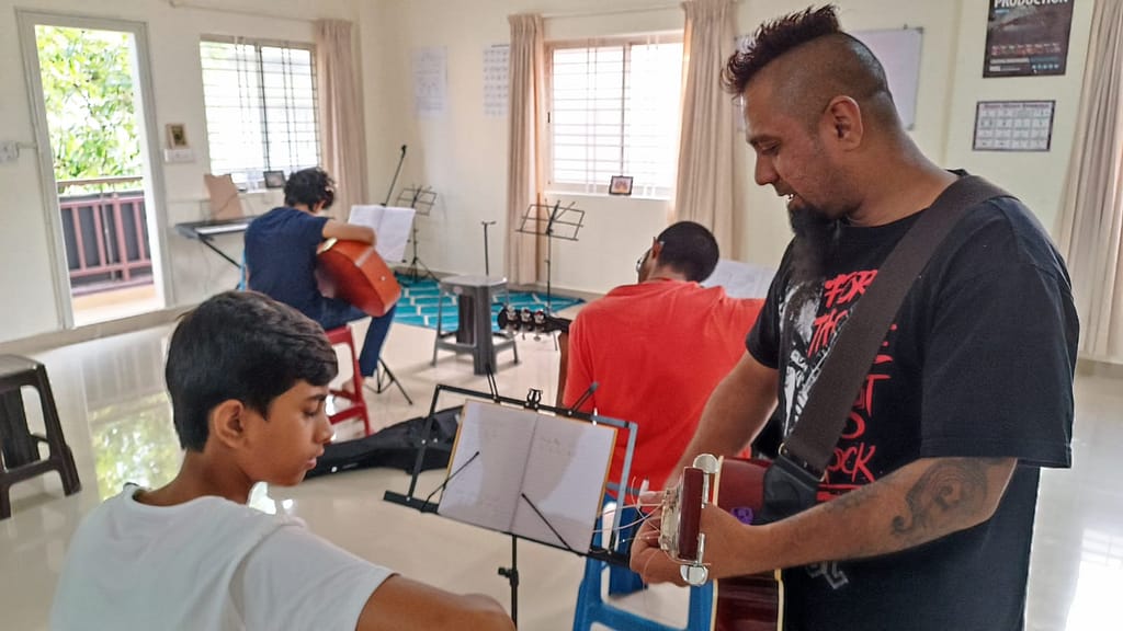 Eric Rodrigues teaching guitar to a student at The First Chord Music & Art School. while students in the back are practicing the guitar