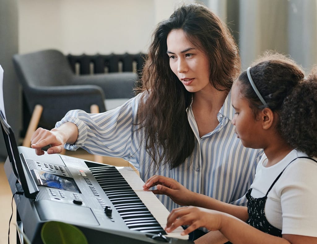 A teacher guiding a student in playing the keyboard during classes