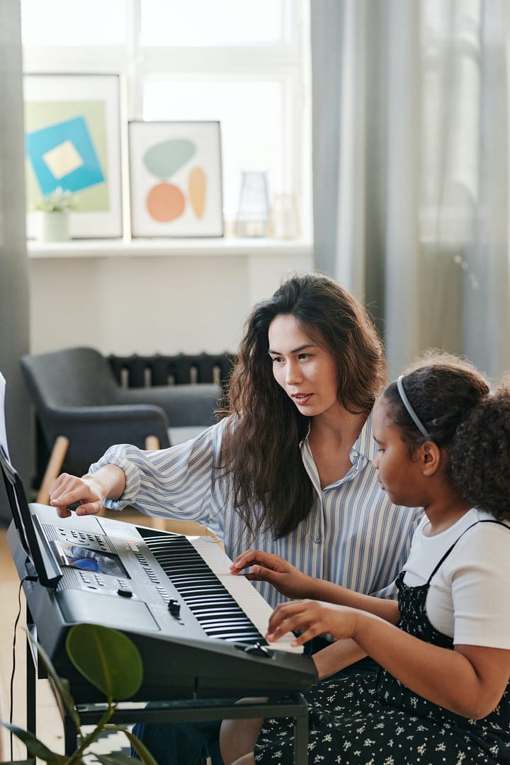 A teacher guiding a student in playing the keyboard during classes