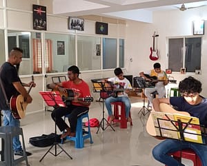 Eric Rodrigues teaching guitar to a student at The First Chord Music & Art School. while students in the back are practicing the guitar