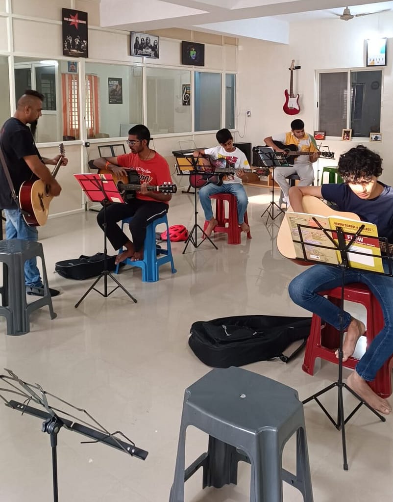 Eric Rodrigues teaching guitar to a student at The First Chord Music & Art School. while students in the back are practicing the guitar