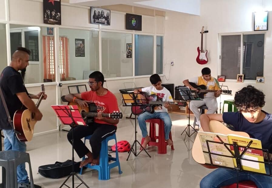 Eric Rodrigues teaching guitar to a student at The First Chord Music & Art School. while students in the back are practicing the guitar