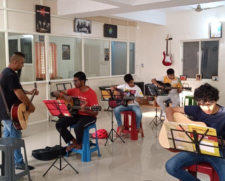 Eric Rodrigues teaching guitar to a student at The First Chord Music & Art School. while students in the back are practicing the guitar