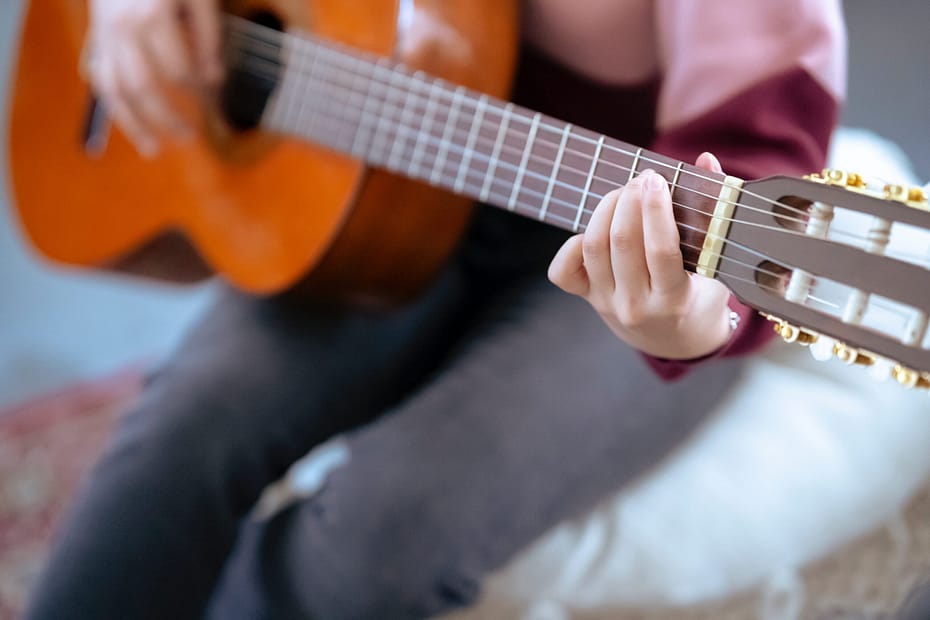 Close-up of a student playing chords on an acoustic guitar.