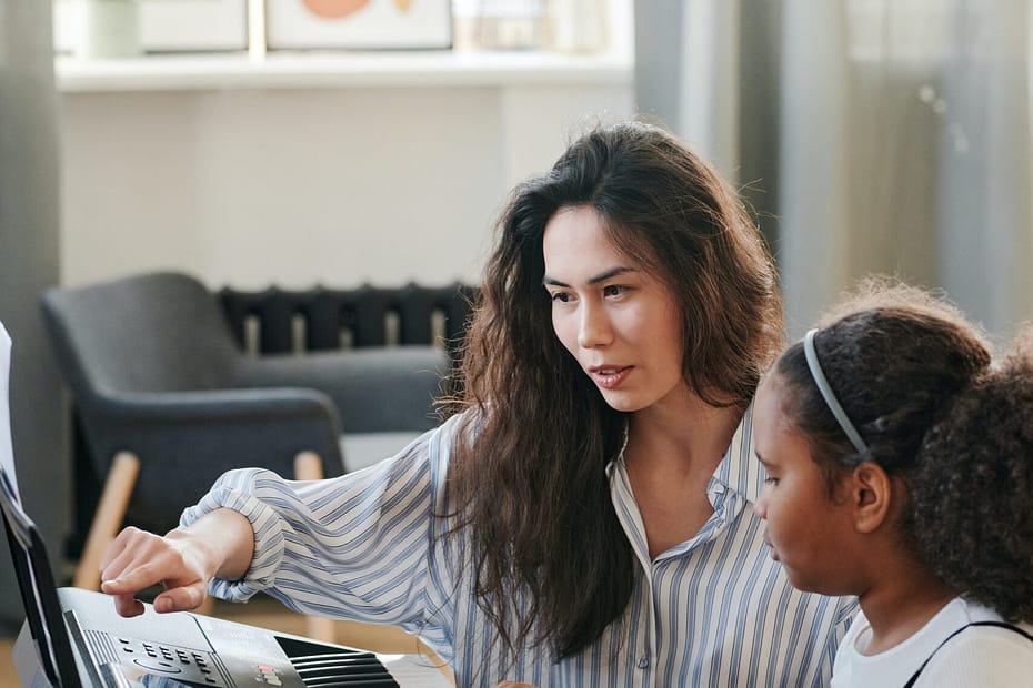 A teacher guiding a student in playing the keyboard during classes